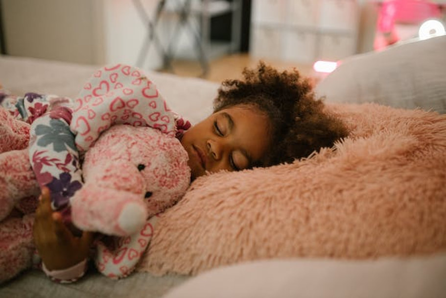 A little girl is sleeping in bed with a stuffed toy in her hands