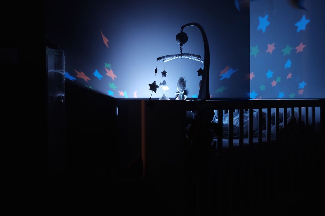 A bed for a baby with a night light on in a darkened room